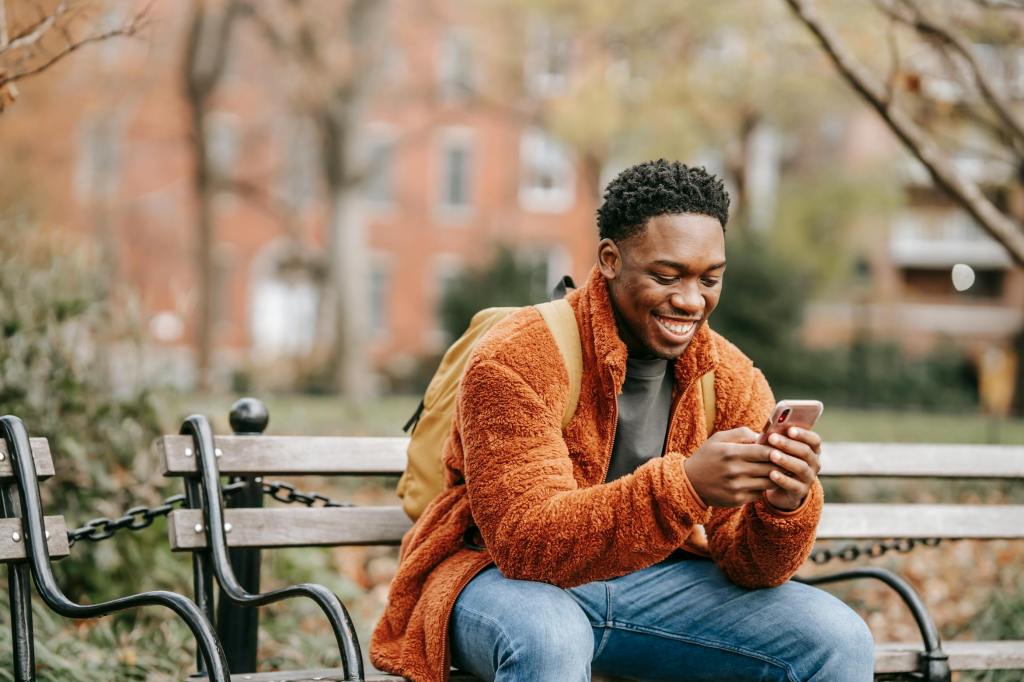 Young Brit sitting on a bench in the US mastering how to stay connected with the perfect phone network.